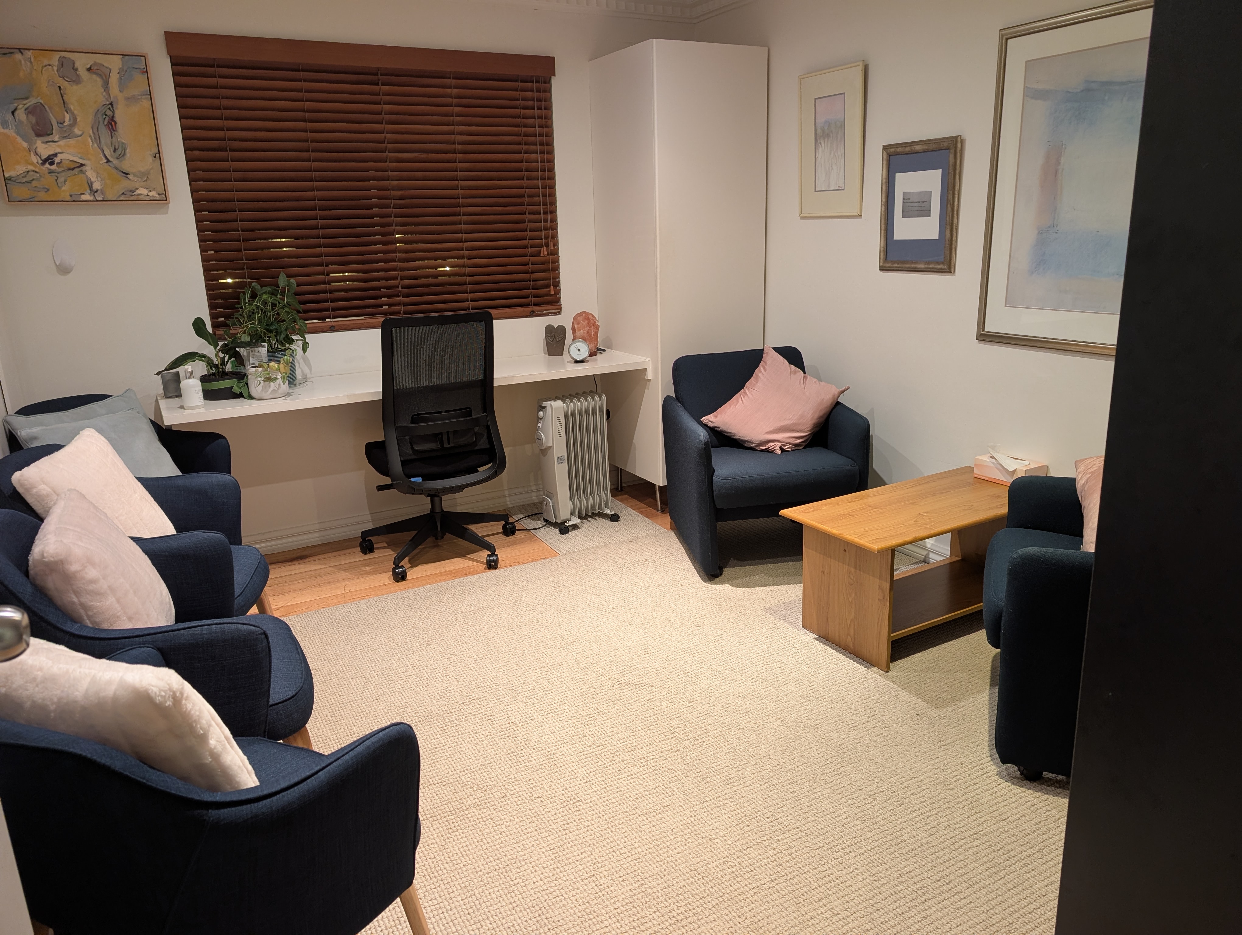 Consulting room at Kew Holistic Health with navy chairs, timber coffee table, and artwork